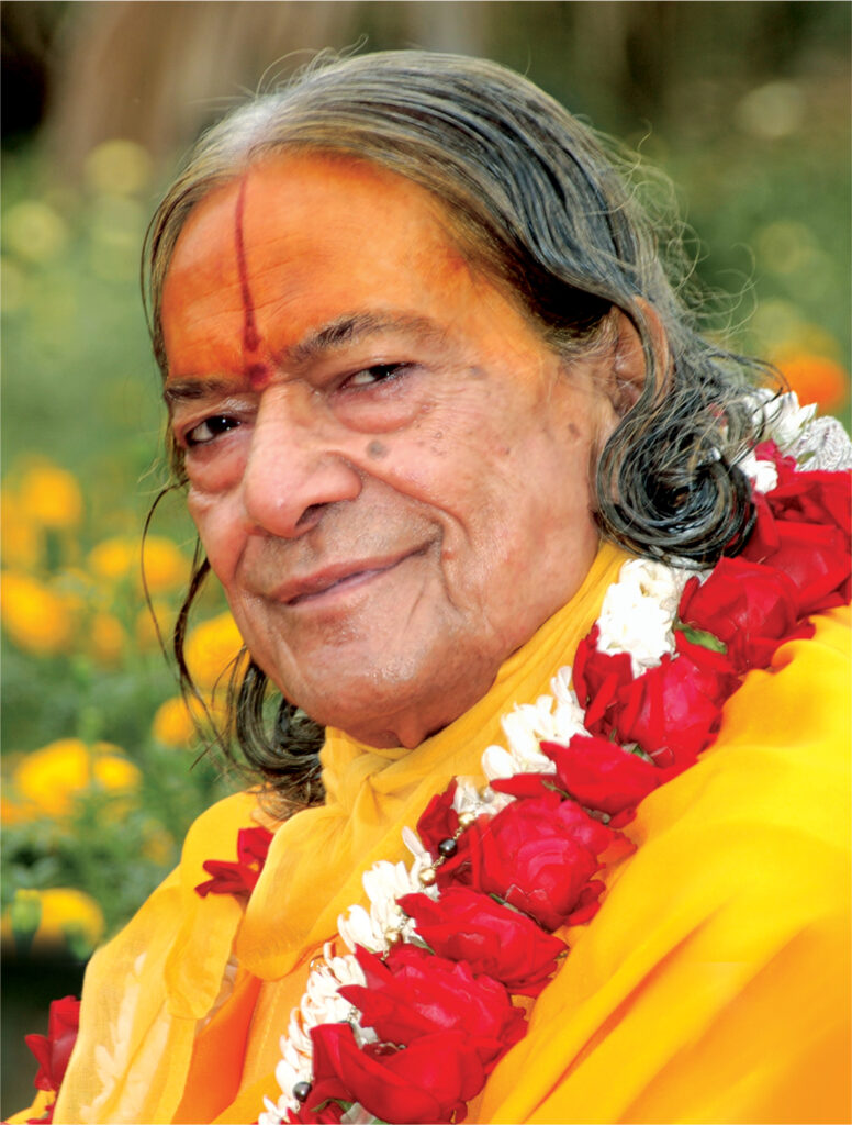 Jagadguru Shri Kripalu Ji Maharaj smiling, wearing a yellow robe and flower garland.